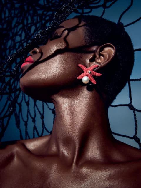 Mulher negra usando brinco em formato de estrela na cor coral com pérola