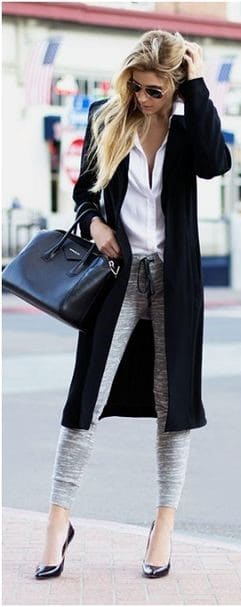 Modelo veste calça moletom cinza, camisa branca, sapato salto fino preto e casaco longo com bolsa no mesmo tom.