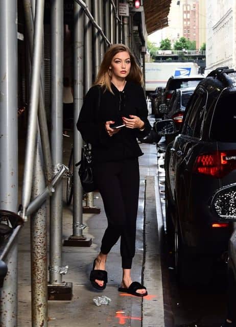 Gigi Hadid veste calça moletom preta, blusa e chinelo slide na mesma cor.