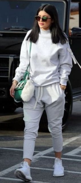 Kylie Jenner veste conjunto cinza de moletom, tênis branco e bolsa de ombro verde.