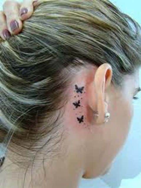 Modelo loira com tatuagem de 3 borboletas pequenas atras da orelha.