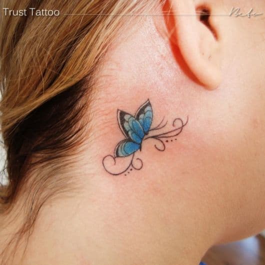 Modelo com tatuagem de borboleta atrás da orelha em tom de azul.