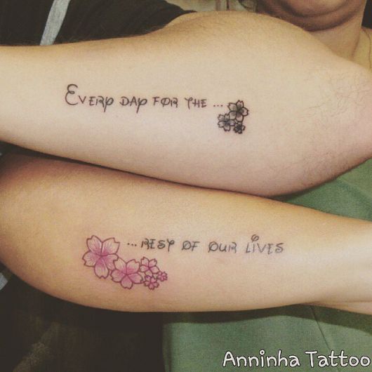 Modelo de tatuagem escrita, no braço com detalhes de flores preto e cor de rosa.