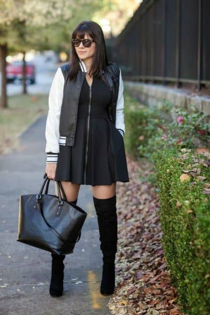 Look com vestido preto, jaqueta preta e branco com detalhe em couro, botas longas na cor preta e bolsa no mesmo tom.