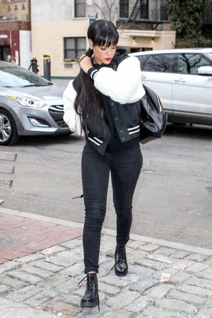 Rihanna veste calça preta, jaqueta na mesma cor com branco, mochila e cuturno também em tons de preto.