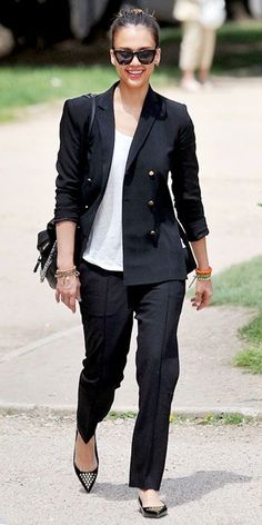 Modelo usa calça preta em alfaiataria, sapatilha preta blusa branca e blazer preto.