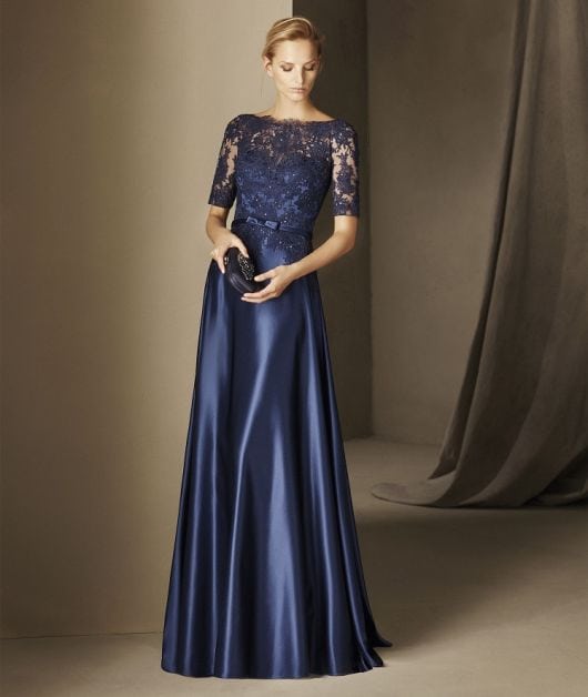 Modelo usa vestido de cetim azul marinho, com mangas e busto em renda.