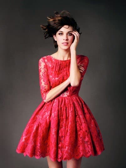 Modelo usa vestido godê vermelho, meia manga de renda.