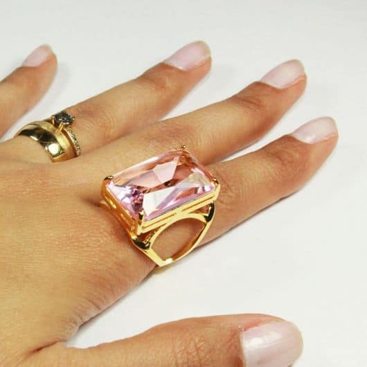 modelo de anel grande com moldura dourada e pedra rosa claro grande.