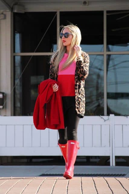 modelo usa calça preta, bota vermelha galocha e casaco de onça com blusa vermelha e rosa.