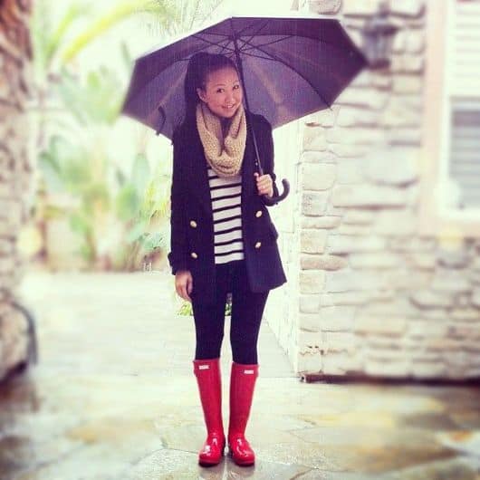 modelo usa calça preta, casaco preto, bota vermelha e blusa listrada em preto e branco.