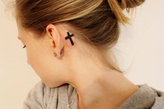 tatuagem, em traço grosso em formato de cruz, atras da orelha.