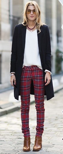 Modelo usa clça vermelha xadrez, blusa branca, casaco preto e bota em cores terrosas.