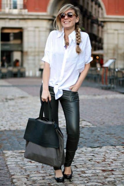 Modelo usa camisa branca, calça de couro preta, sapatilha e bolsa na mesma cor.