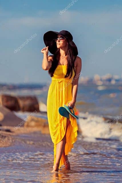 Modelo veste vestido amarelo vibrante com chapéu de praia preto.