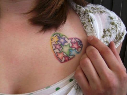 Tatuagem no ombro de um coração com varias estrelas coloridas em seu interior
