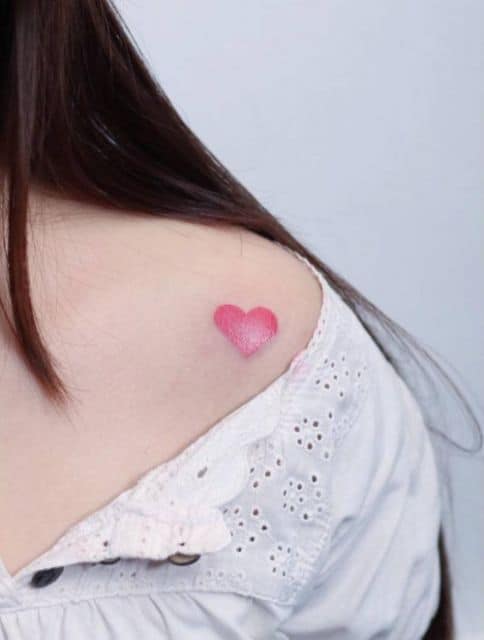 Tatuagem de um coração pintado de rosa no ombro de uma mulher