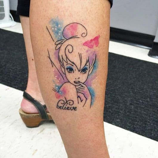 Tatuagem da Sininho da perna com tons de azul e rosa, acompanhada da frase "Believe"