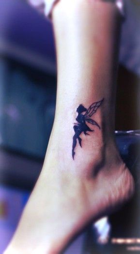 Tatuagem pequena de uma fada pintada de preto olhando para cima no tornozelo
