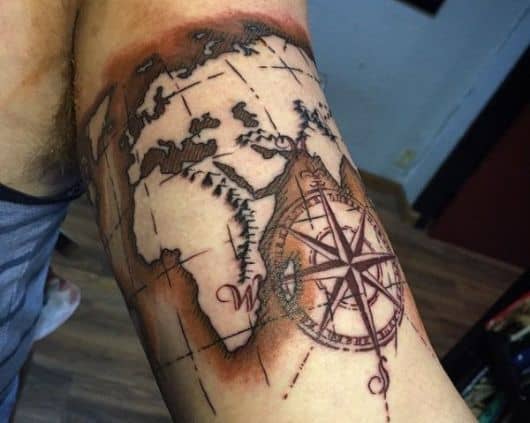 Tatuagem de uma bússola próxima ao Mapa Mundo com bastante sombreamento 