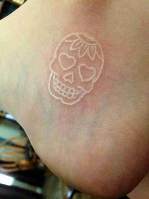 Tatuagem branca de uma caveira mexicana no calcanhar 
