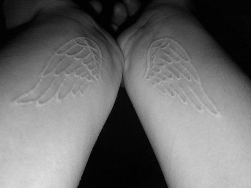 Duas tatuagens brancas de asa, uma em cada perna