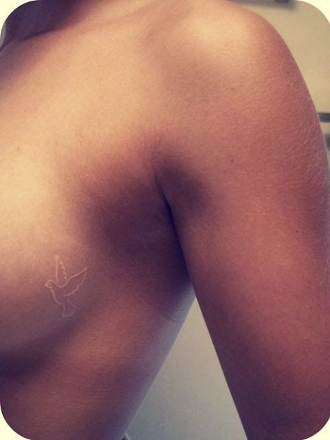 Tatuagem branca de uma pomba muito pequena na lateral do seio de uma mulher