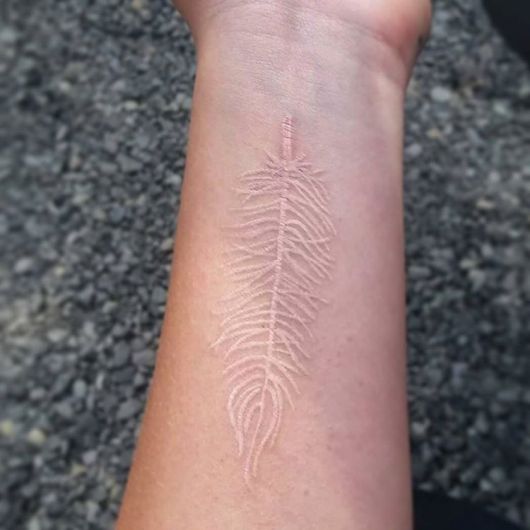 Tatuagem branca de uma pena no antebraço de uma pessoa