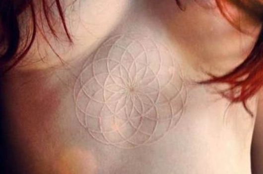 Tatuagem branca de vários círculos interligados entre os seios de uma mulher