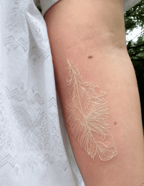 Tatuagem branca no braço de uma pessoa de uma pena voltada para baixo