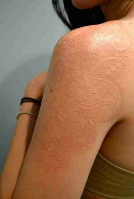 Tatuagem branca que cobre a parte superior do braço, principalmente o ombro