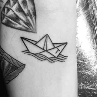 Tatuagem de um barco de papel muito pequeno com um T escrito em sua lateral