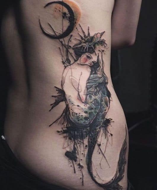 Tatuagem na costela de uma sereia sentada olhando para trás com a lua próxima dela.