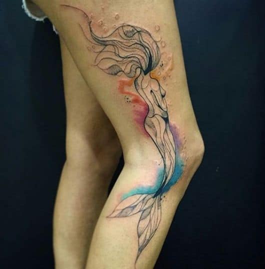 Tatuagem na perna de uma sereia feita em aquarela olhando para o horizonte