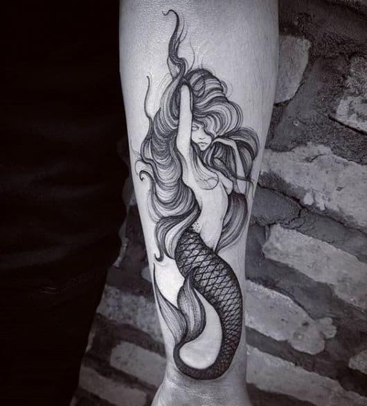 Tatuagem de uma sereia misteriosa feita em preto e branco no antebraço.