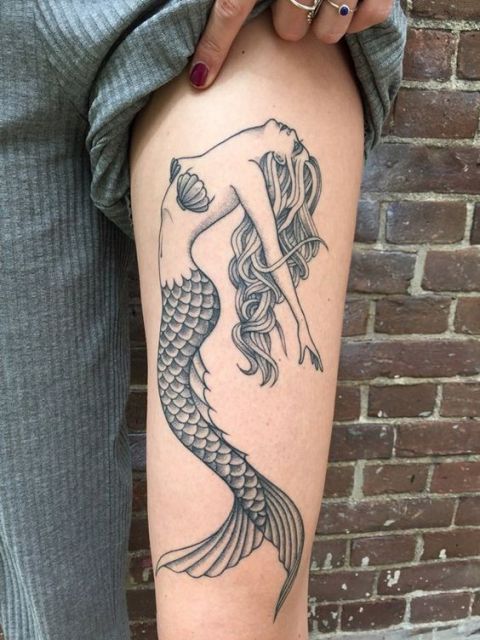 Tatuagem de uma sereia com conchas cobrindo os seios vista de lado e olhando para cima