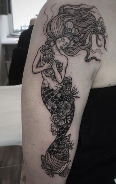 Tatuagem em preto e branco de uma sereia com diversos adornos floridos em sua cauda e nos cabelos.