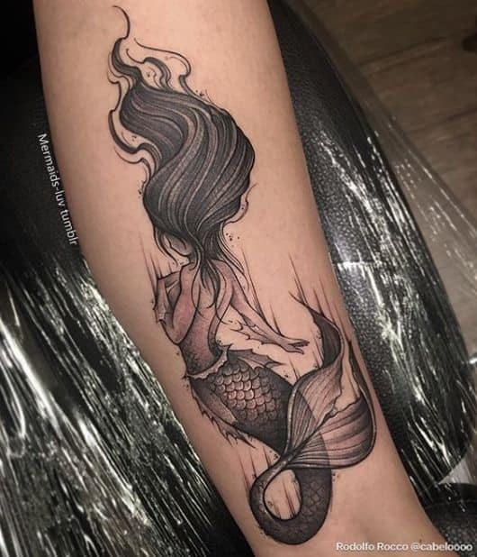 Tatuagem de uma sereia vista de costas com os cabelos grandes e soltos balançando