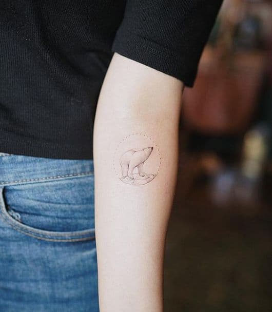 Tatuagem pequena no antebraço de um urso polar dentro de um círculo