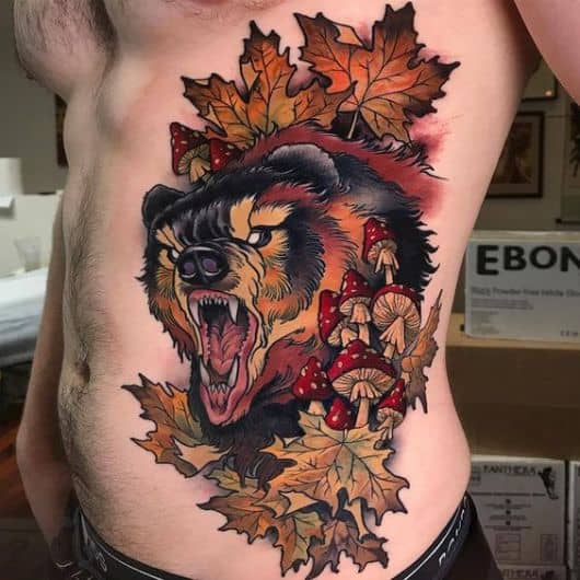Tatuagem na barriga de um urso rugindo em meio a folhas secas