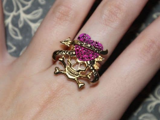 Modelo de anel de caveira de ouro com detalhes de coração cor de rosa.