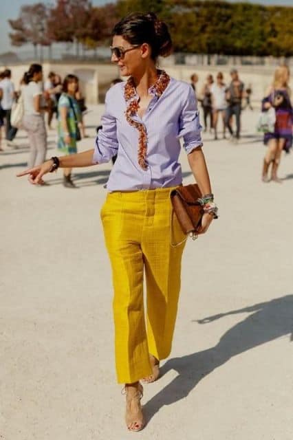Modelo usa camisa lisa lilás, calça amarela, bolsa e sapato.