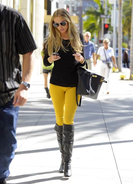 Modelo usa calça amarela, bolsa preta, bota e blusa na mesma cor.