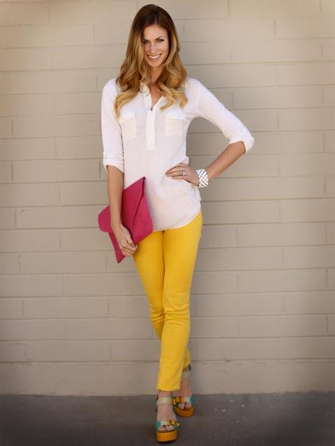 Modelo usa calça amarela, bolsa rosa, camisa branca e sandalia.