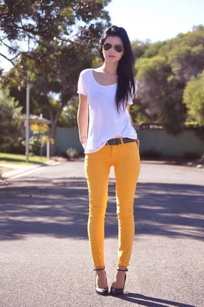 Modelo usa calça amarela com cinto, sapato e camisetinha branca.