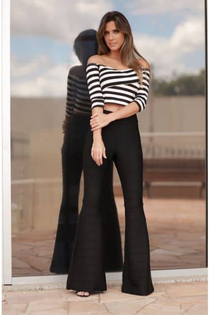 Modelo usa calça preta flare, blusa cropped listarda em preto e branco.