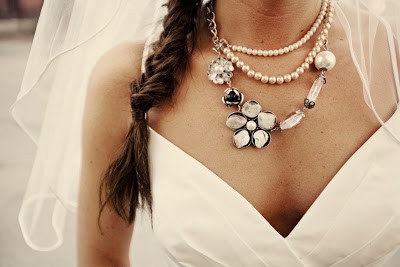 Modelo usa vestido branco decotado e colar com pérolas e pingente de flores.