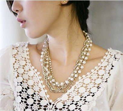 Modelo usa colar de pérola branco com dourado e prata com blusa branca de broderie na gola.