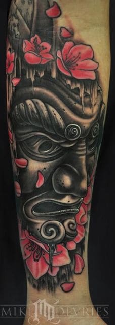 Tatuagem de uma máscara samurai com aspecto zangado e folhas vermelhas ao seu redor. 
