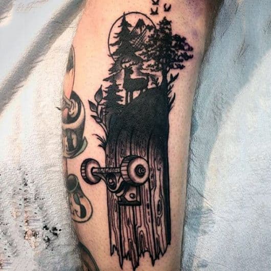 Tatuagem de um skate partido ao meio em preto e branco com uma floresta e um cervo no topo